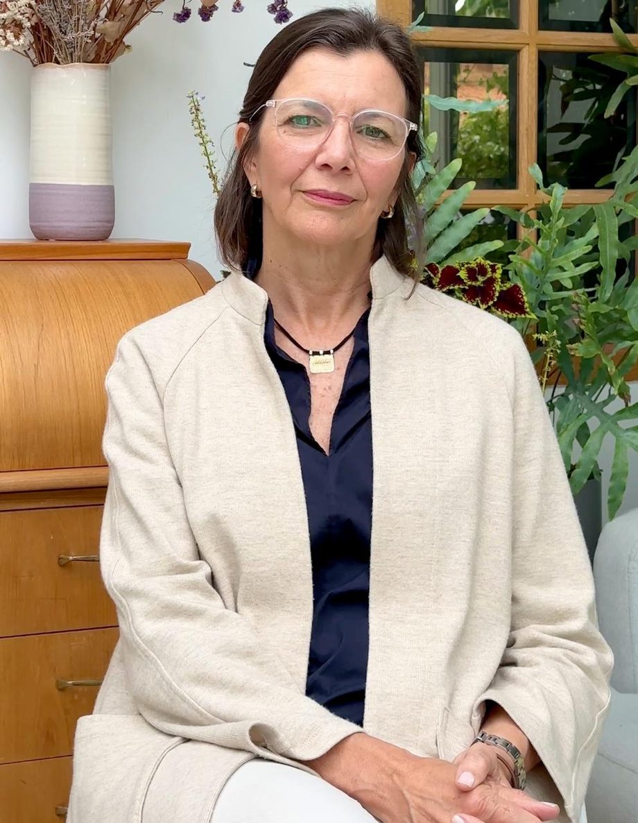 Carolina Barrios, sentada, con una chaqueta clara, ante una ventana y unas plantas